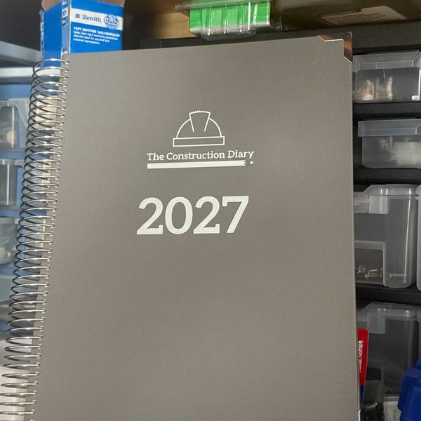 Gray notebook titled 'The Construction Diary' with '2027' on a workbench with tools and supplies.